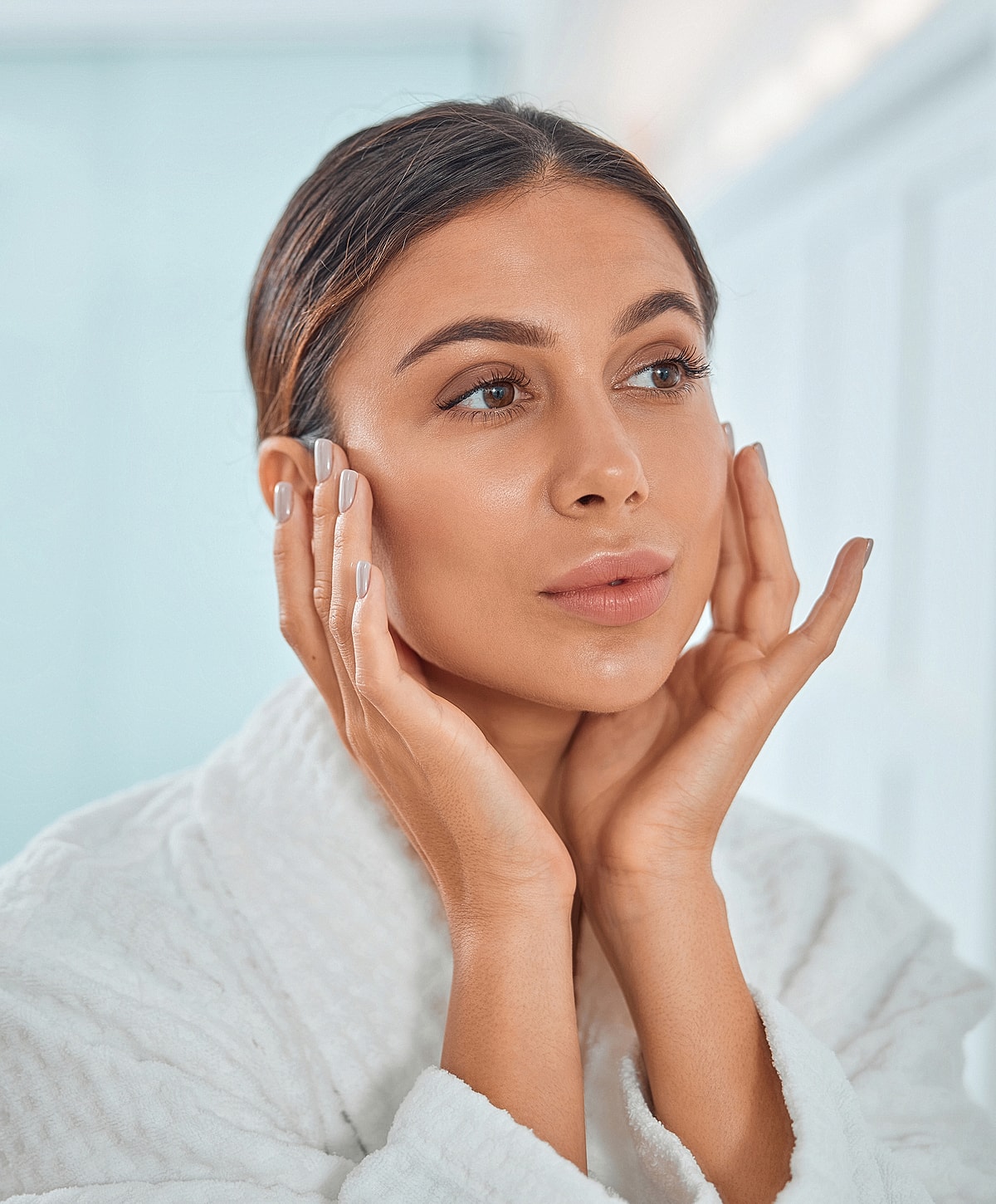 Woman in robe touching her face gently.